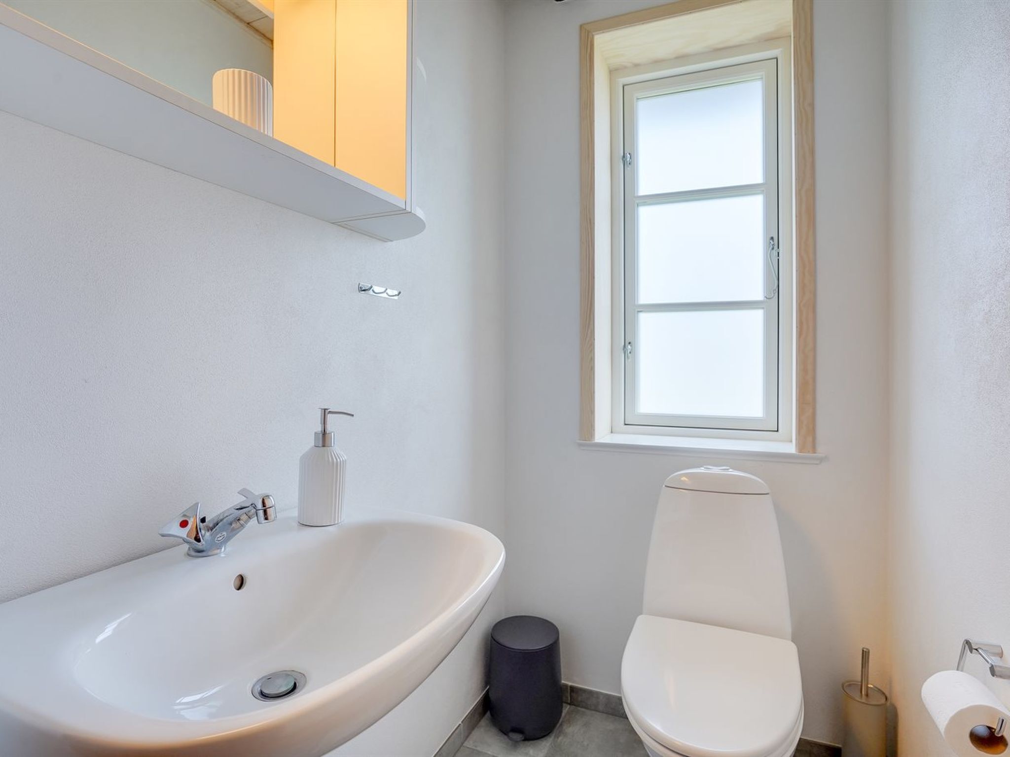 A modern bathroom with a white sink, toilet, and window.