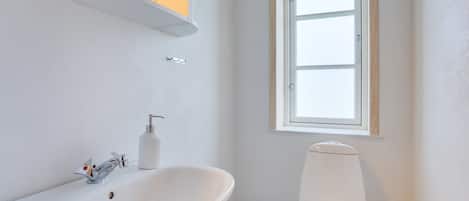 A modern bathroom with a white sink, toilet, and window.