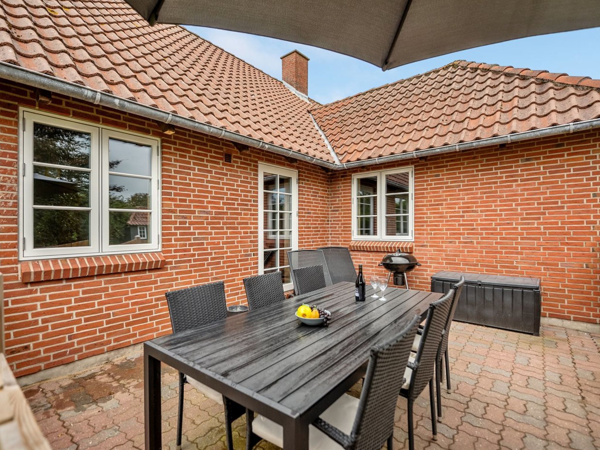 Un patio con una casa de ladrillo, una mesa con sillas y una parrilla.