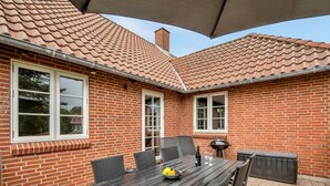 Un patio con una casa de ladrillo, una mesa con sillas y una parrilla.