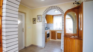 A kitchen with a tiled floor, wooden cabinets, a built-in oven, and a window with curtains. - Vineyard cottage Cvitkovič (Crnomelj)