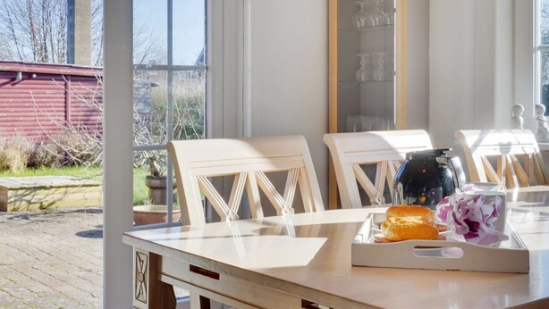 A dining area with a table set for two, a bread roll, and a cup.