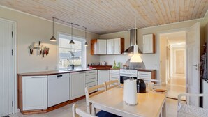 A modern kitchen with white cabinets, a wooden dining table, and pendant lighting.