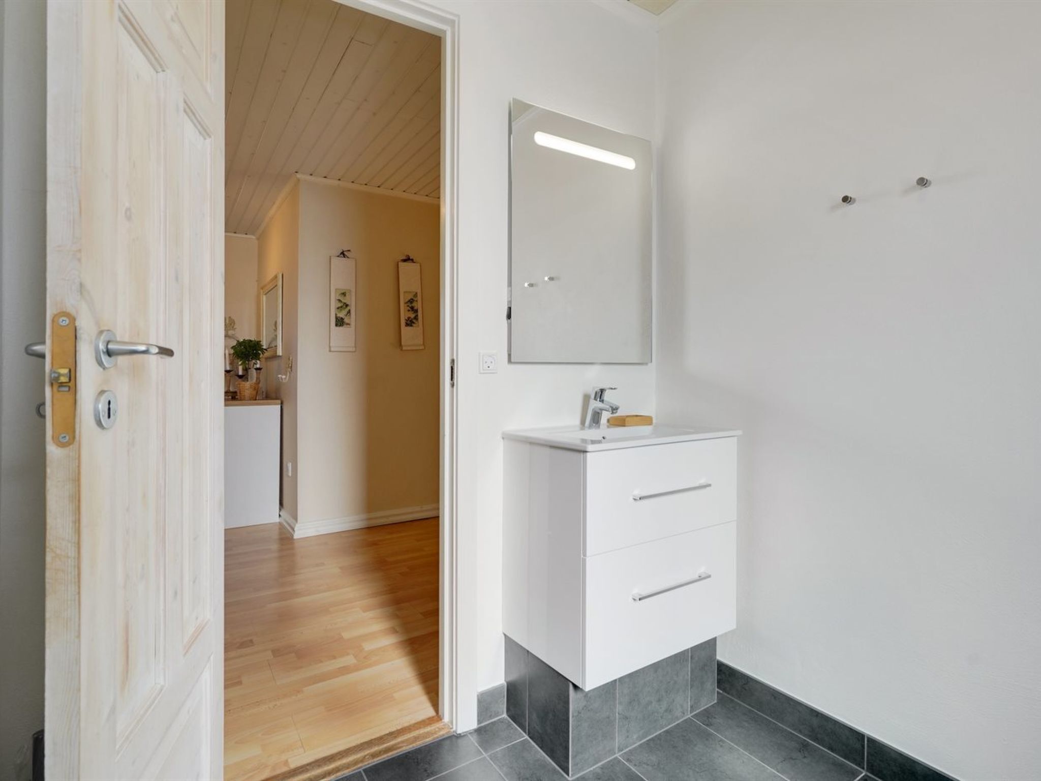 Une salle de bain moderne avec un meuble-lavabo blanc, un miroir et une porte en bois.
