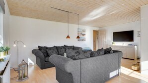 A modern living room with a grey sectional sofa, wooden flooring, a flat-screen TV, and pendant lighting.
