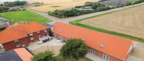 A red-roofed building with a patio area, surrounded by fields and a road.