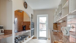 Cocina moderna con encimeras de granito, electrodomésticos de acero inoxidable y vista al jardín trasero a través de una puerta abierta.