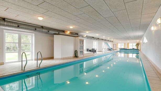 Una piscina interior con agua cristalina, paredes con azulejos e iluminación empotrada en el techo.