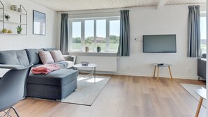 Ein modernes Wohnzimmer mit einem grauen Sofa, einem kleinen runden Tisch und einem an der Wand montierten Fernseher.