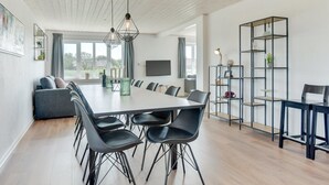 Ein moderner Essbereich mit einem langen Tisch, schwarzen Stühlen und Pendelleuchten.