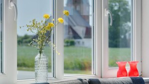 Ein Fenster mit freiem Blick auf ein Kirchturm und grüne Vegetation.
