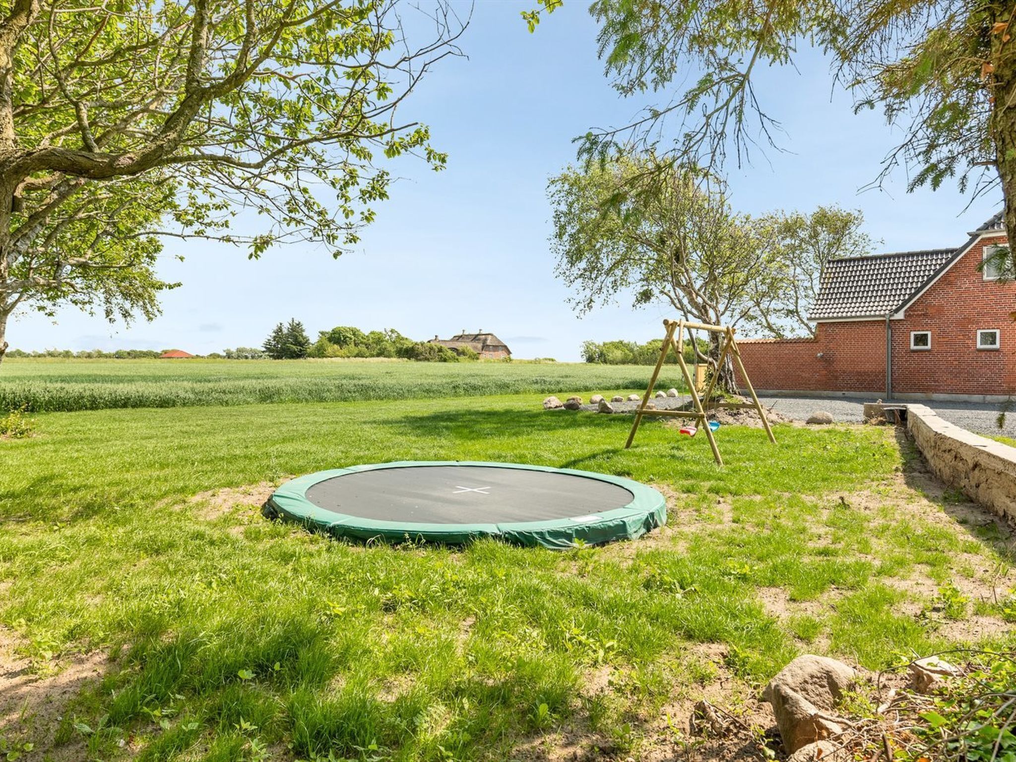 Un espace extérieur verdoyant avec un trampoline, une balançoire et un bâtiment en briques en arrière-plan.