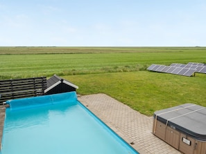 Una piscina con bordo in legno, una sauna e pannelli solari in un ambiente rurale.