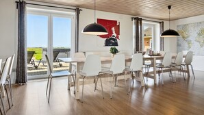 A modern dining area with white chairs and a wooden table, large windows with curtains, and a world map on the wall.