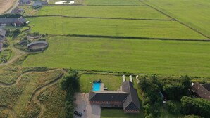 An aerial view of a rural property with a large green field, a swimming pool, and a house with a sloped roof.