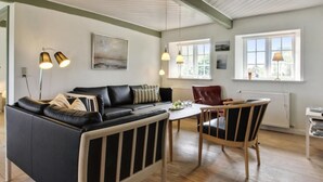 A modern living room with a black leather sofa, wooden dining table, and chairs. There are pendant lights, a radiator, and large windows providing natural light. - "Ingulf" - 18km from the sea by Interhome (Bredebro)