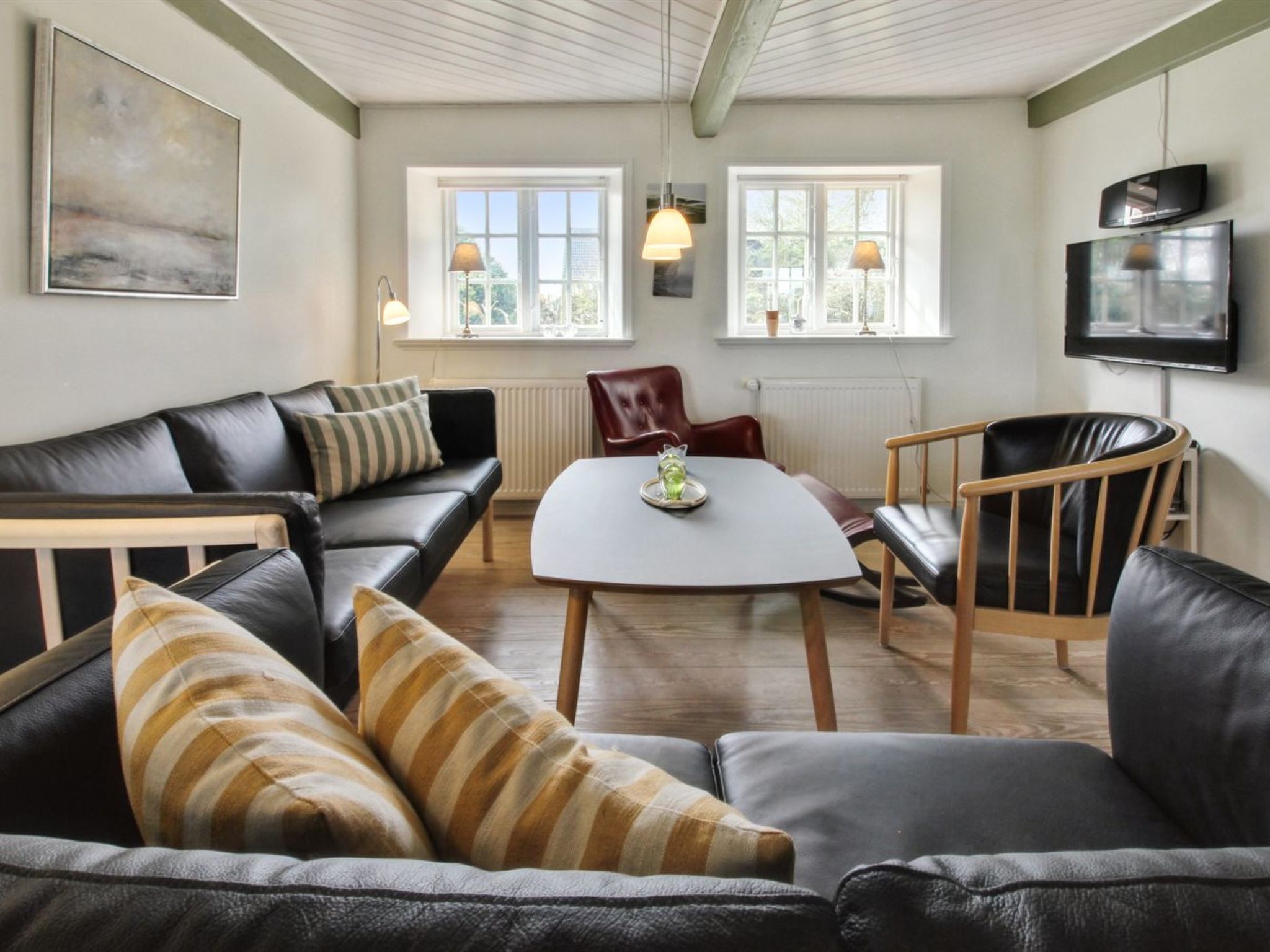 Un salon moderne avec un canapé en cuir noir, une table à manger en bois et un téléviseur fixé au mur.
