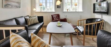 Un salon moderne avec un canapé en cuir noir, une table à manger en bois et un téléviseur fixé au mur.