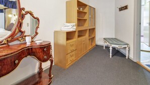 Ein Hotelzimmer mit einem Holznächtigstisch, einem großen Spiegel, einem Schrank aus Holz, einer Bank und einer Tür zu einem weiteren Raum.