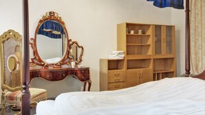 Ein Himmelsbett mit Holz-Kopfstück, ein großer, verziertes Spiegel, ein Holzschrank und ein Sessel mit dekorativer Rückenlehne.