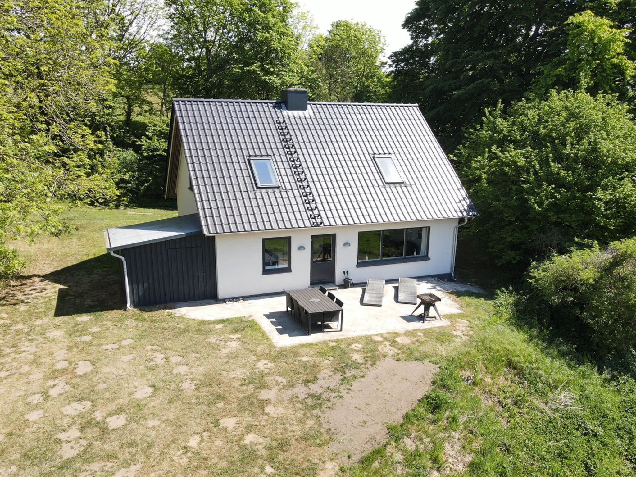 Une maison moderne à deux étages, dotée d’un toit en pente, d’un patio couvert avec coin salon extérieur et d’une grande fenêtre au deuxième étage.