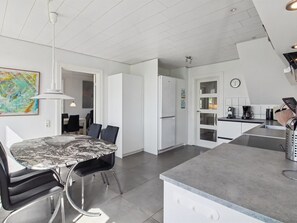 A modern kitchen with a marble-top dining table, white cabinetry, and a built-in oven.