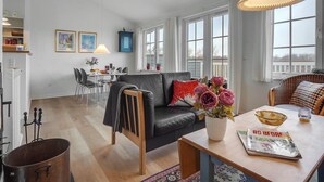 A modern living room with a sofa, dining table, and chairs. There are large windows, a lamp, and a blue cabinet.