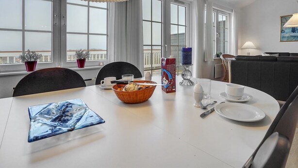 A dining area with a white table, chairs, a decorative lamp, and a view of the outside through large windows.