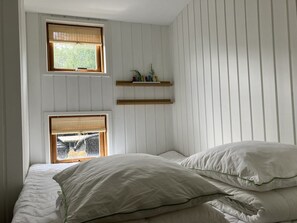 Un dormitorio con dos ventanas, estanterías de madera y una cama con ropa de cama blanca.