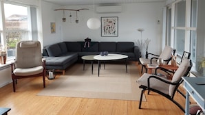 Ett modernt vardagsrum med en hörnsoffa, ett runt soffbord och en matplats med ett litet bord och stolar.