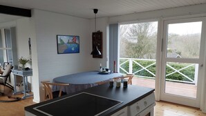 Ett modernt kök med en central köksö, en matplats med bord och stolar samt en stor skjutdörr i glas som leder ut till en terrass.