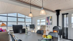 Ein moderner Essbereich mit großem Tisch, Stühlen, Kamin und Blick durch große Fenster.