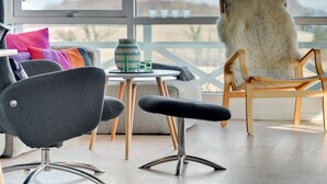 Ein modernes Wohnzimmer mit einem grauen Sessel, einem Holzstuhl und einem kleinen Tisch mit einer Vase und Gläsern.