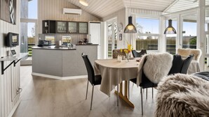 A modern kitchen with a central island, a dining area with a round table, and a view of the outdoors.