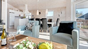 Een moderne woonkamer met een houten plafond, een eethoek en een keuken op de achtergrond.