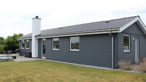 Uma casa moderna térrea com fachada cinza, chaminé e um espaço de varanda com móveis de exterior.