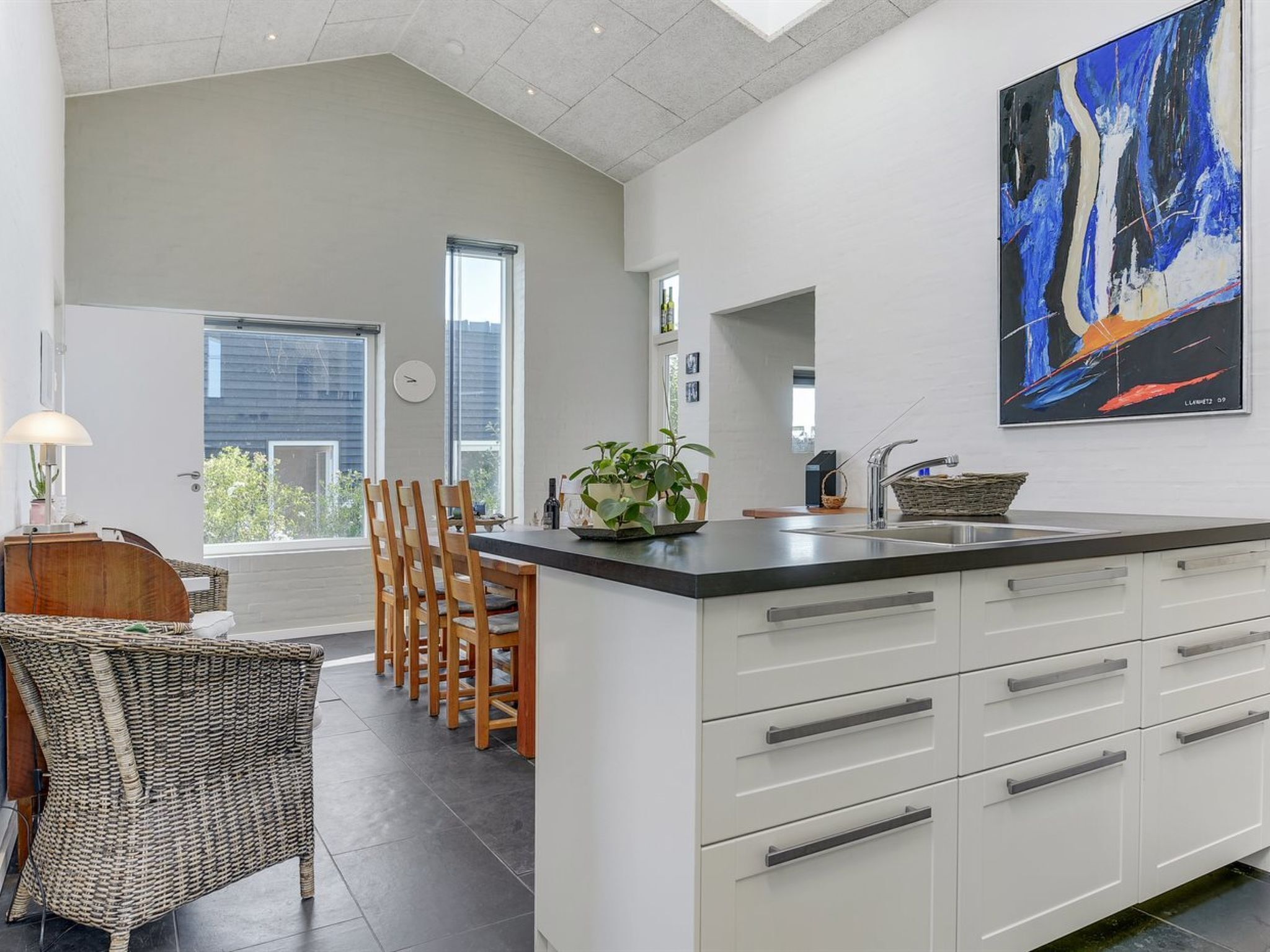 A modern kitchen with a large island, white cabinetry, and a large abstract painting on the wall.