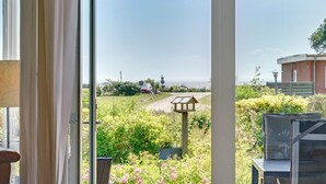Blick durch eine Glastür auf einen Garten mit einem Weg, einer hölzernen Konstruktion und einem Gebäude im Hintergrund.