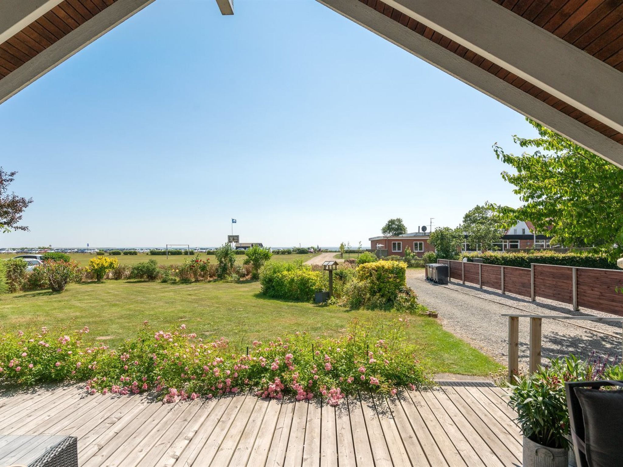 Une terrasse en bois offrant une vue sur une zone verdoyante, une maison en briques et un ciel dégagé.