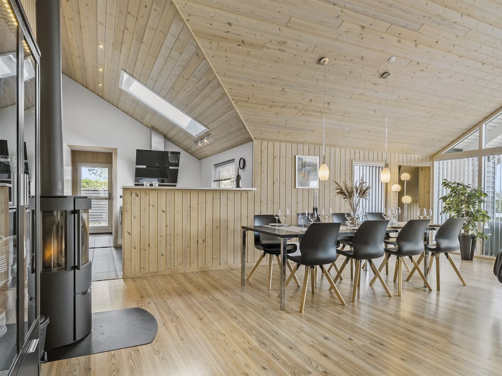 Une salle à manger spacieuse avec un plafond en bois et de grandes fenêtres, une cuisine équipée d’appareils modernes et une cheminée.