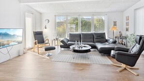 Un salon moderne comprenant un canapé d’angle, deux fauteuils, une table basse et un téléviseur à écran plat.
