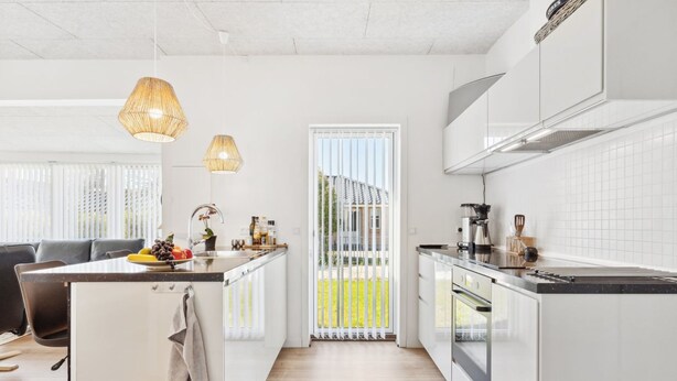Une cuisine moderne dotée d’un îlot central, d’un coin repas avec un canapé et d’une vue sur l’extérieur grâce à une porte coulissante.