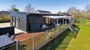 Une maison moderne dotée d’un patio couvert, d’une terrasse en bois et d’un petit jardin.