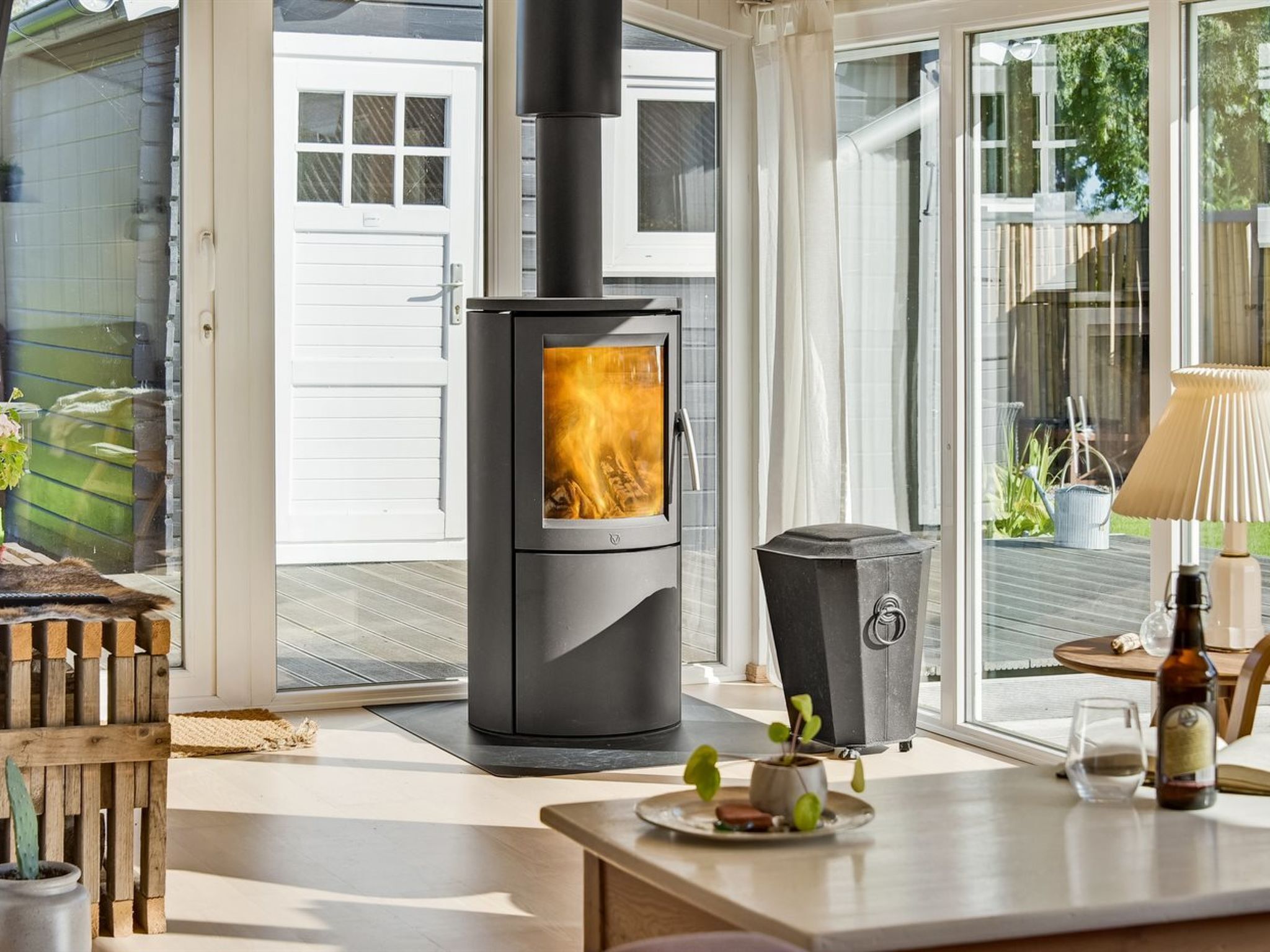 Een moderne keuken met een houtkachel, een eethoek met een tafel en stoelen, en uitzicht op buiten.
