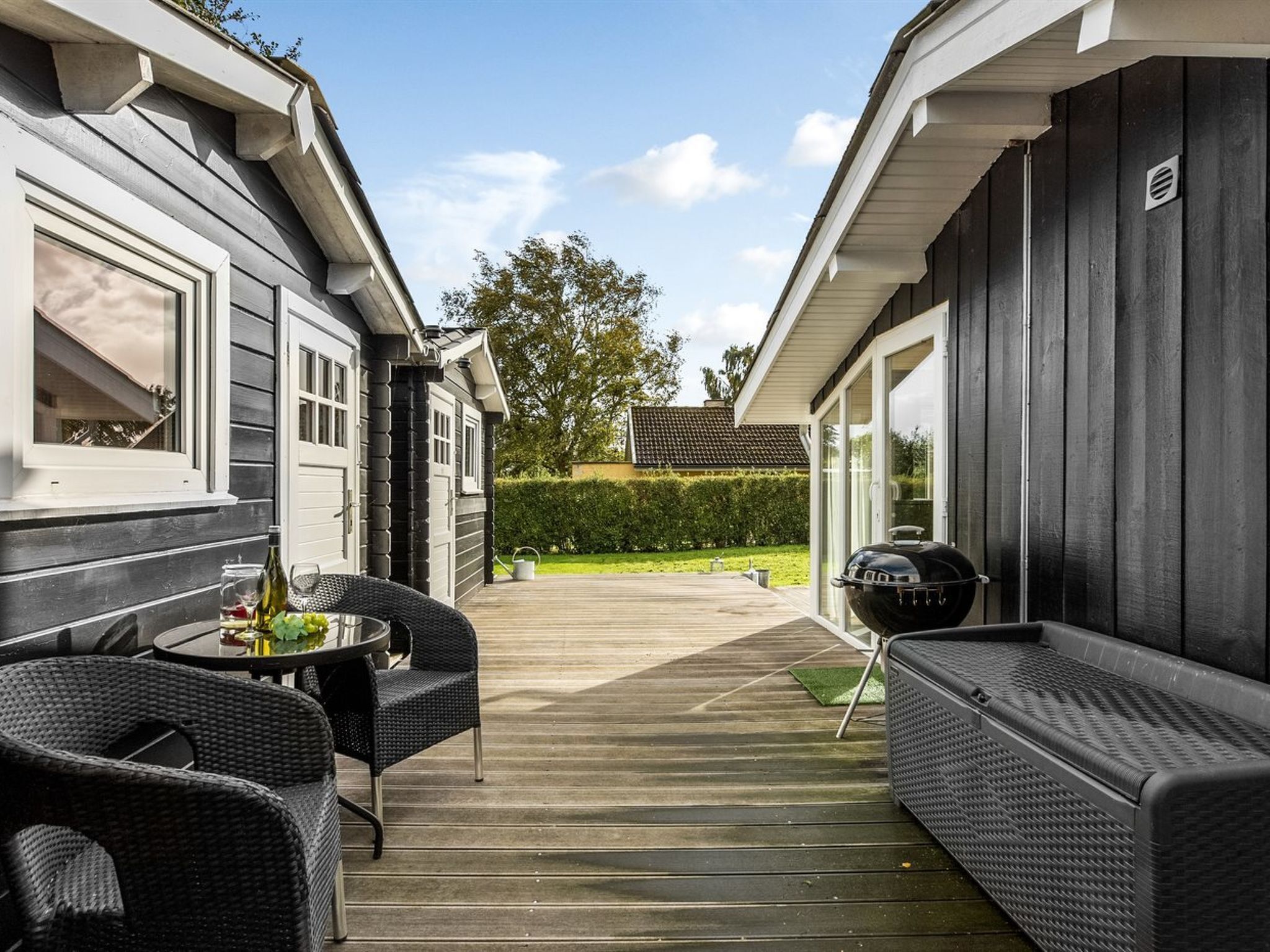 A covered patio with wicker furniture, a grill, and a view of a neighboring house.