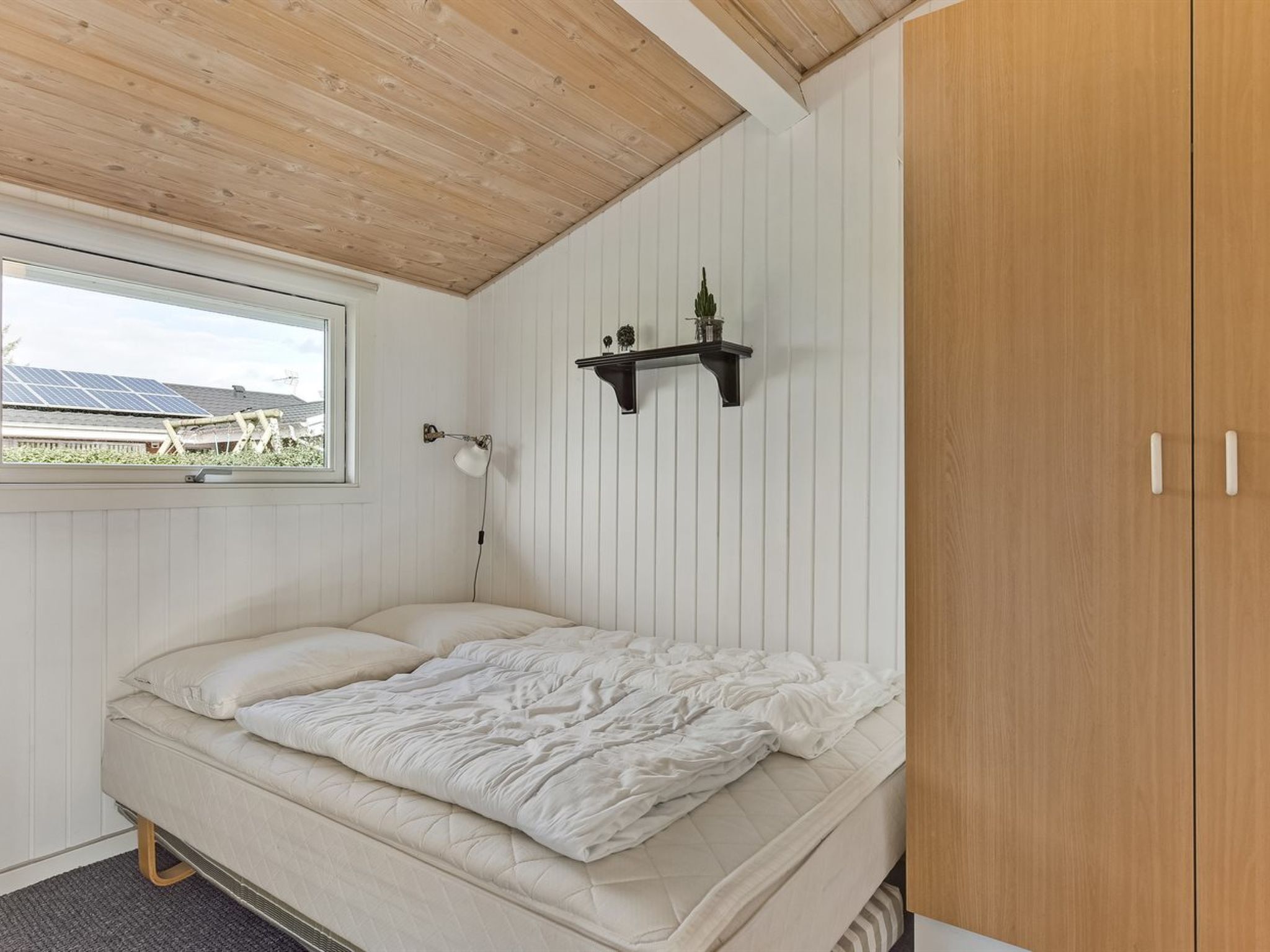Un dormitorio con cama, ventana, estante montado en la pared y armario.