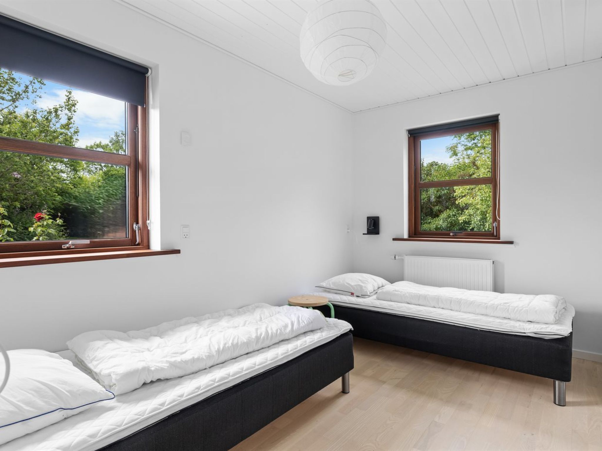 Ein modernes Schlafzimmer mit zwei Einzelbetten, einem kleinen Tisch und großen Fenstern mit Blick auf Grünflächen.