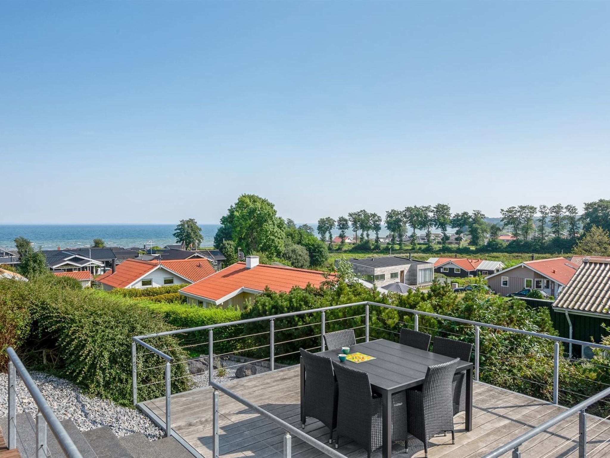 Eine Dachterrasse mit Tisch und Stühlen, mit Blick auf eine Küstenlandschaft mit Häusern und Bäumen.