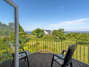 Una terraza de madera con dos sillas, vista a una casa y al mar.