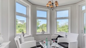 Una habitación luminosa con tres ventanas amplias, sillas de mimbre, una mesa de cristal y un candelabro.